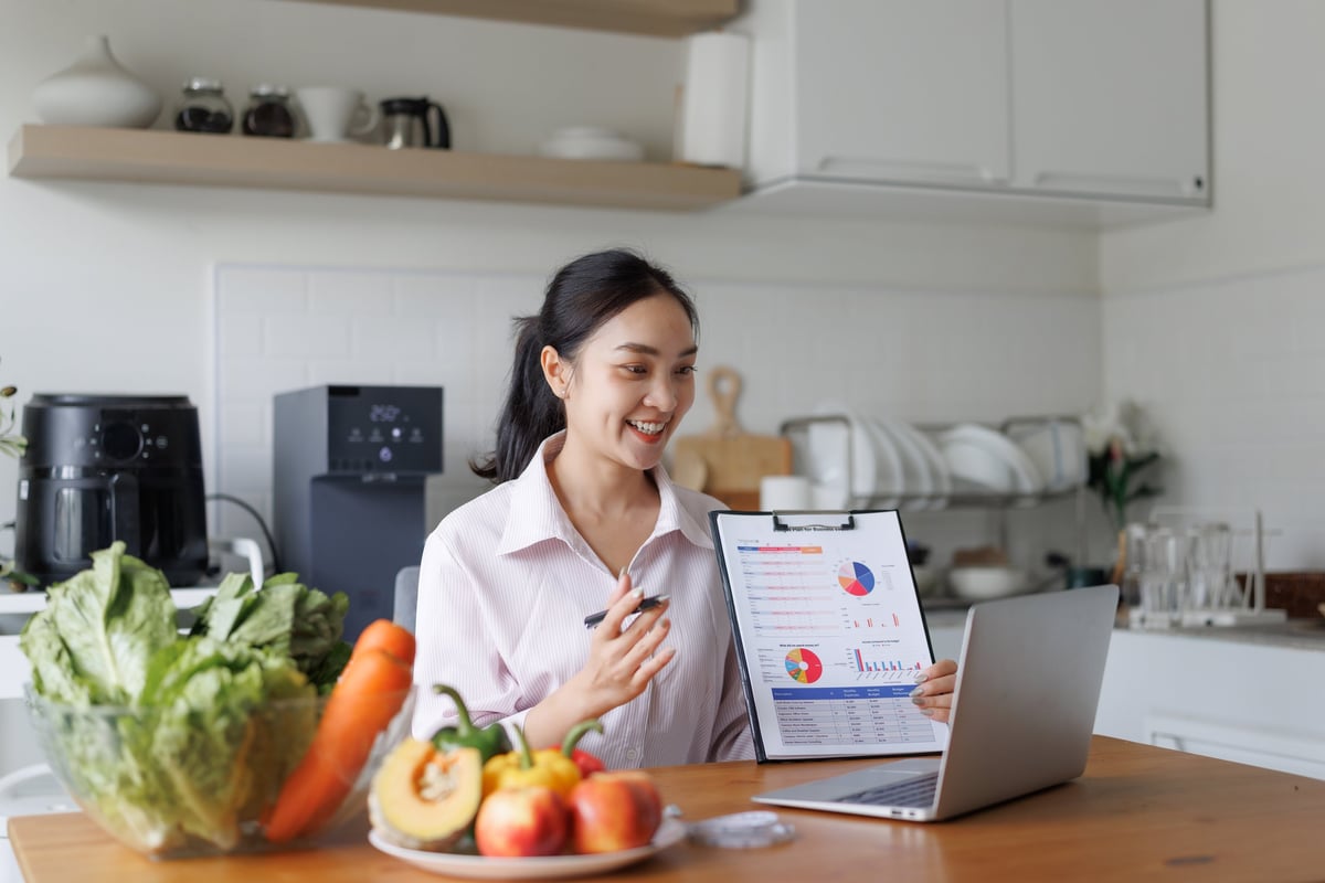 Woman presenting healthy diet data and business reports on laptop during a video conference in her modern kitchen